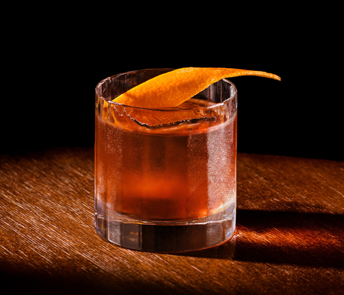 Bowmore Old Fashioned Cocktail im Glas mit Orangenzeste garniert auf einem Holztisch