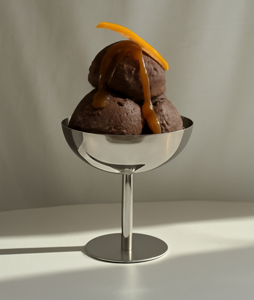 Smoky Chocolate Sundae mit KSchokoladensoße und Orangenzeste in einem Eisbecher aus Metall, vor einem grauen Hintergrund