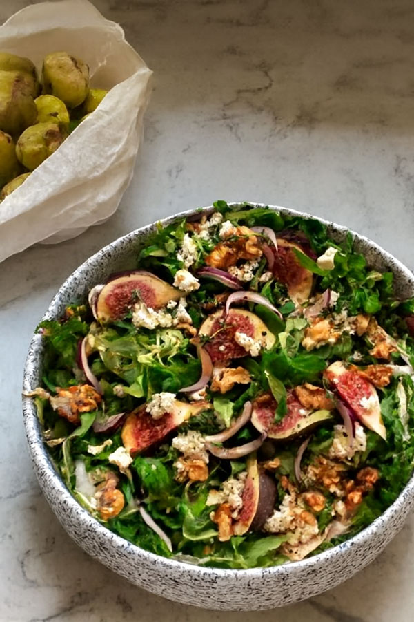 Feldsalat mit Feigen und Ziegenkäse in einer grauen Schüssel auf einem Marmortisch