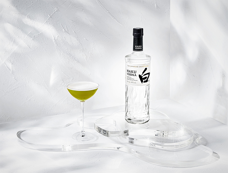 Grüner Haku Matcha Martini Cocktail im Glas neben einer vollen Falsche Haku Vodka vor weißem Hintergrund