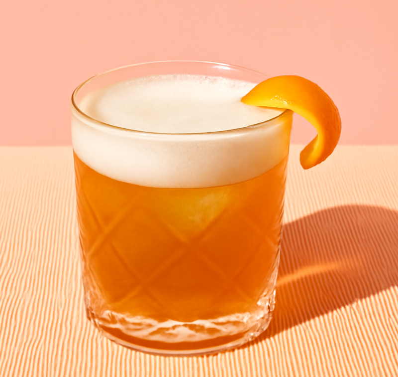 Laphroaig Sour Cocktail garniert mit Zitronenzeste im Glas auf einem orangenen Untergrund