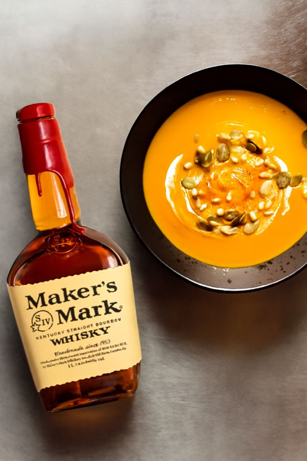Eine Flasche Maker's Mark neben einem teller Kürbissuppe garniert mit Kürbiskernen