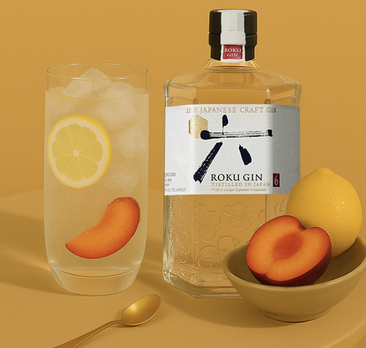 Roku Momiji Fizz Cocktail im Glas mit Scheiben von Pflaume und Zitrone, sowie Eiswürfeln, neben einer Flasche Roku Gin und einer Schale mit Zitrone und Orange