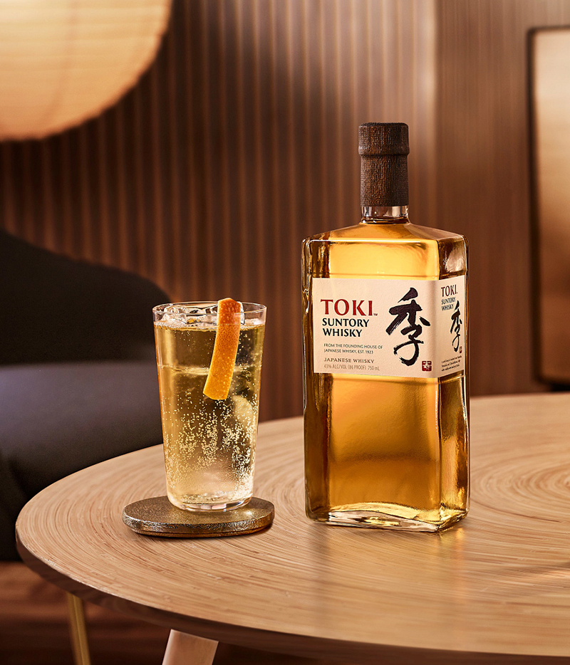 Toki Highball im Glas mit einer Grapefruit-Scheibe neben einer vollen flasche Suntory Toki Whisky auf einem Holztisch