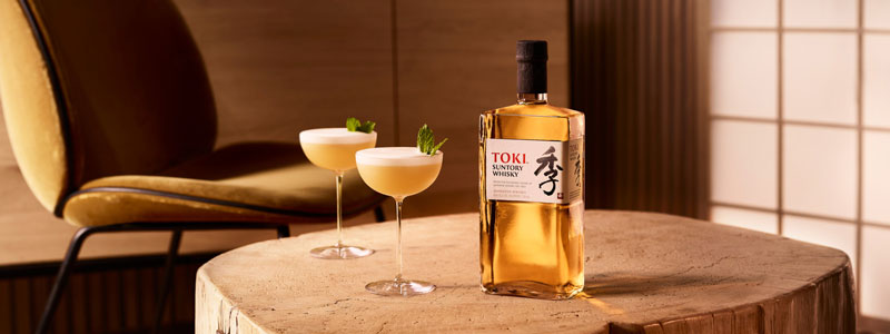 Toki Whisky Flasche und zwei Gläser mit dem Cocktail Toki Sour auf einem Holz-Tisch