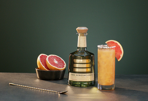 Tre Paloma Cocktail mit Zuckerrand und Grapefruitscheibeneben einer Flasche Tre Generaciones, einem Löffel und einer Schale mit zwei Grapefruit-Hälften