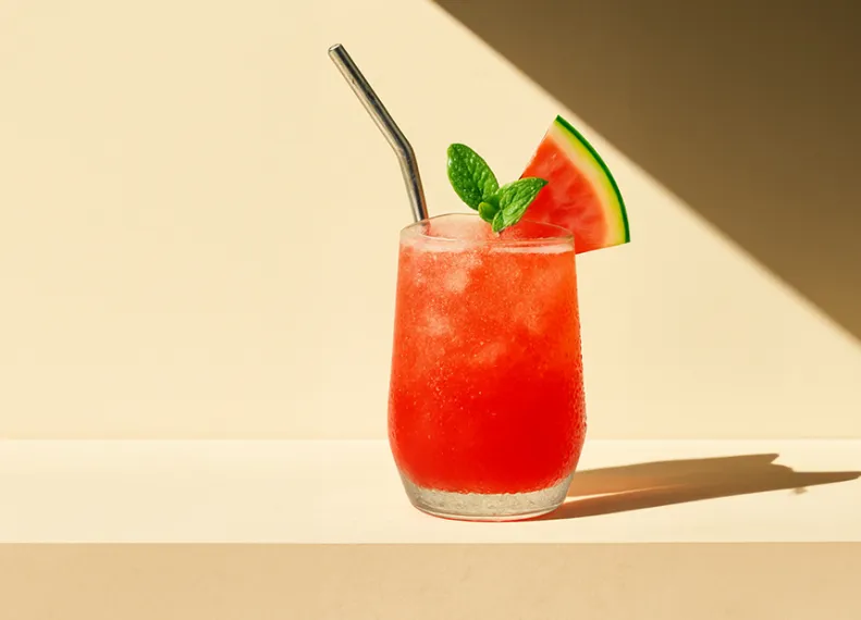 Roter Haku Velvet Sunset Cocktail in einem Glas, garniert mit Minzblättern und einer Melonenscheibe