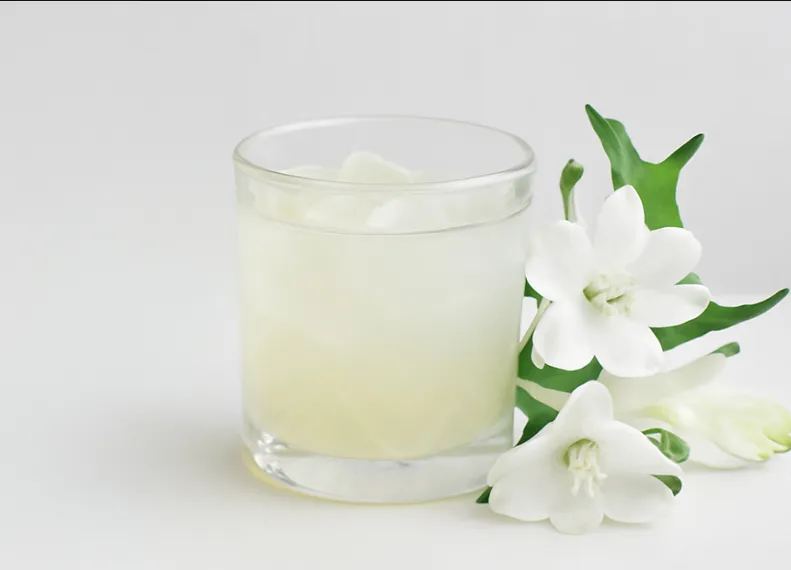 Roku Cocktail im Glas mit Eis neben einem Zweig mit weißen Blüten