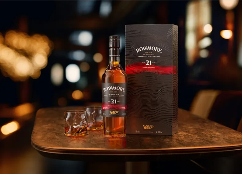 Bowmore Sherry Oak Cask 21 Years Old Flasche und Karton neben 2 gefüllten Gläsern auf einem Holztisch