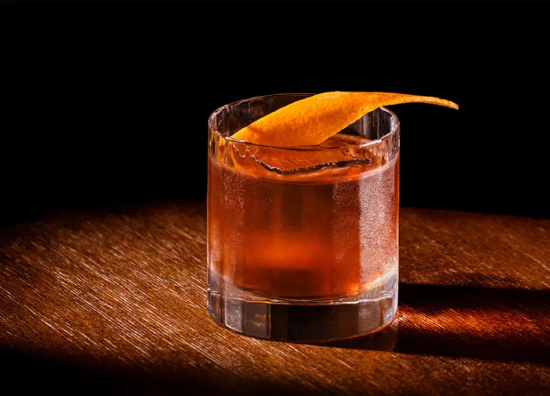 Bowemore Old Fashioned Cocktail im Glas mit Orangenzeste garniert auf einem Holztisch
