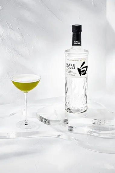 Haku Matcha Martini Cocktail im Glas neben einer Flasche Haku Vodka vor weißem Hintergrund