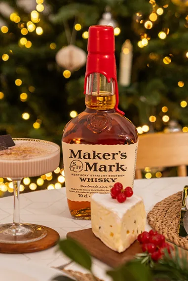 Maker's Mark Bourbon und Cocktail auf einem festlich gedeckten Tisch mit Teller vor einem geschmückten Weihnachtsbaum