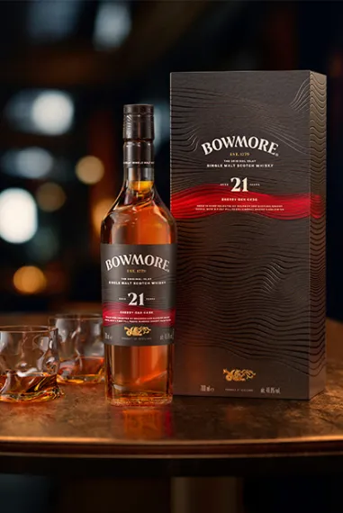 Bowmore Sherry Oak Cask 21 Years Old Flasche und Karton neben 2 gefüllten Gläsern auf einem Holztisch