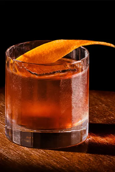Bowemore Old Fashioned Cocktail im Glas mit Orangenzeste garniert auf einem Holztisch