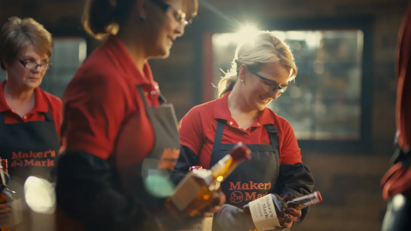 Two female workers dip bottles of Maker's Mark whiskey in hot red wax to seal them