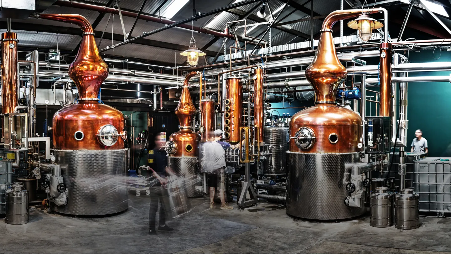 Industrial space filled with shining metal and copper coloured distillery equipment.