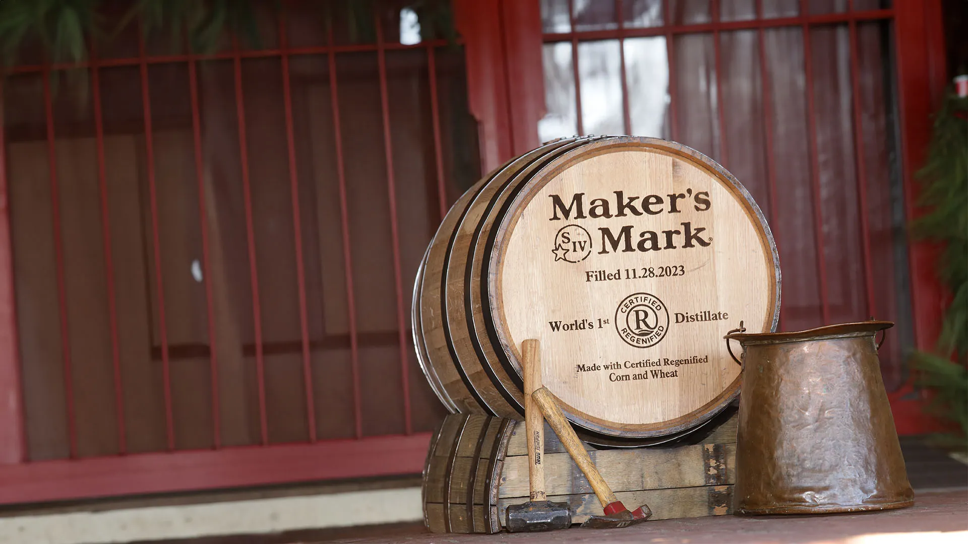 A Maker's Mark whiskey barrel beside a  large copper vessel. Two hammers are propped against the barrel.