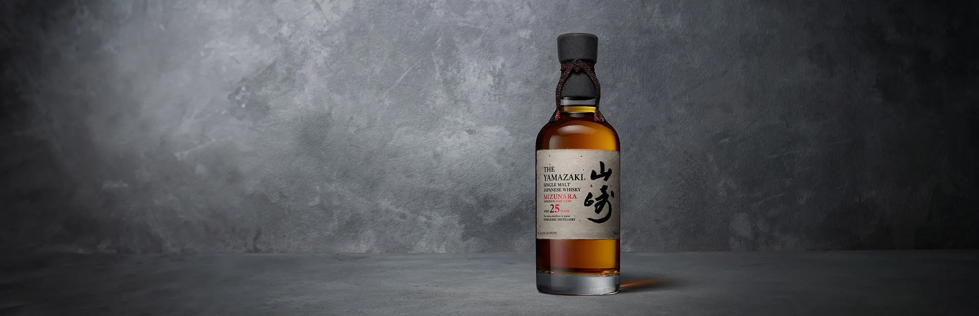 Eine Flasche aYmazaki 25 Years Old Mizunara vor einem dunklen grauem Beton-Hintergrund