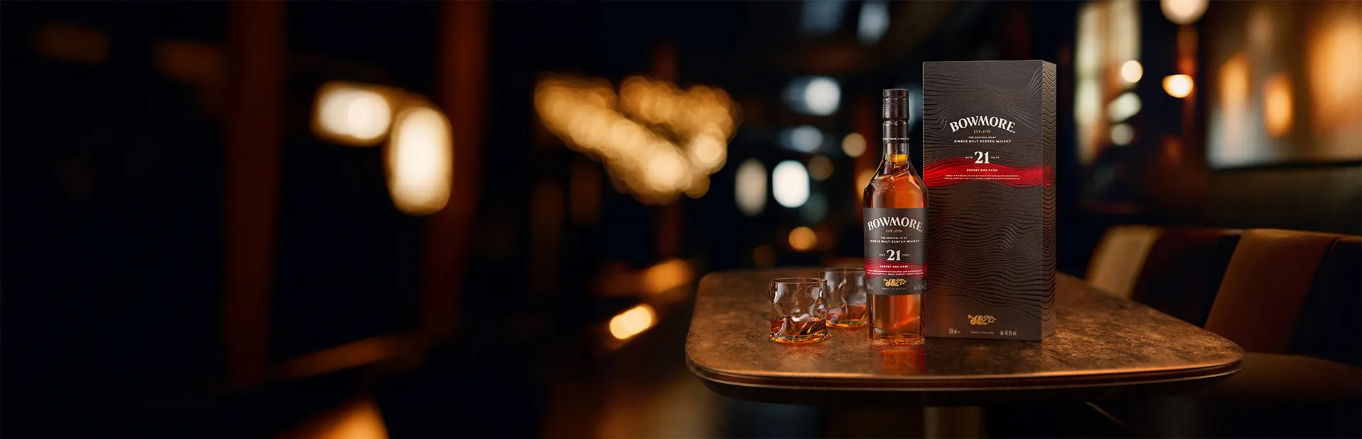 Bowmore Sherry Oak Cask 21 Years Old Flasche und Karton neben 2 gefüllten Gläsern auf einem Holztisch