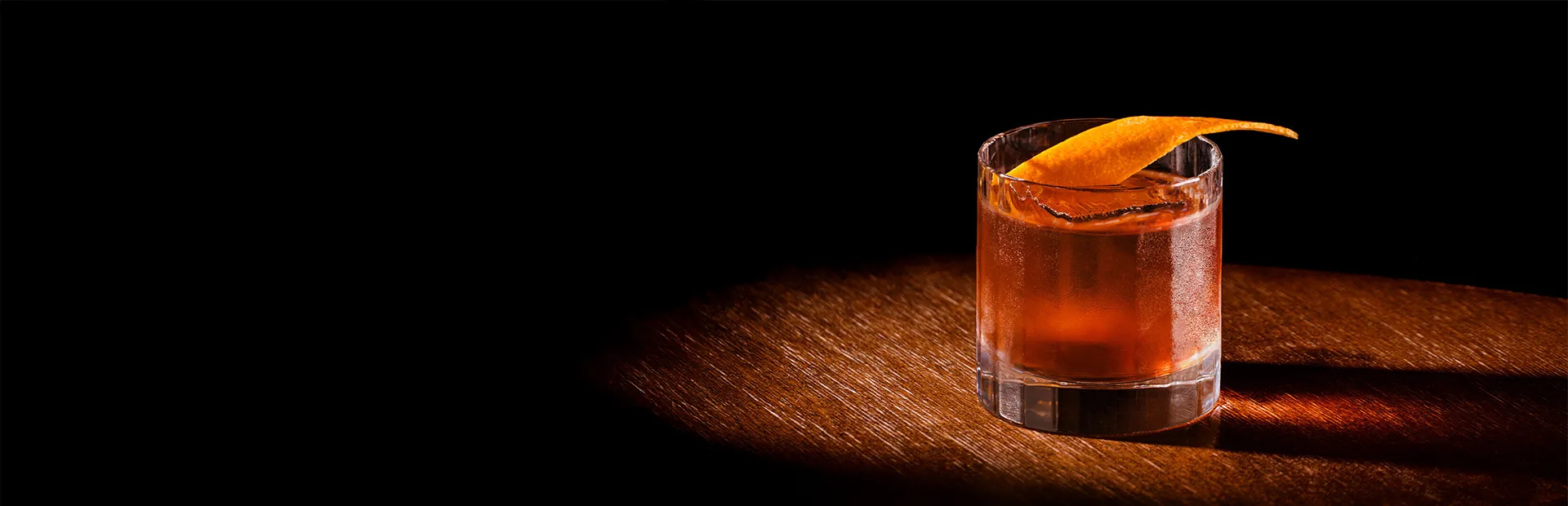 Bowemore Old Fashioned Cocktail im Glas mit Orangenzeste garniert auf einem Holztisch